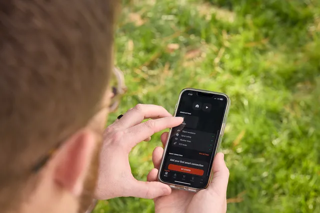 Person using Husqvarna Automower app beside a lawn
